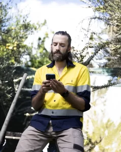 A man wearing a neon yellow high-vis shirt looks angrily down at his phone.